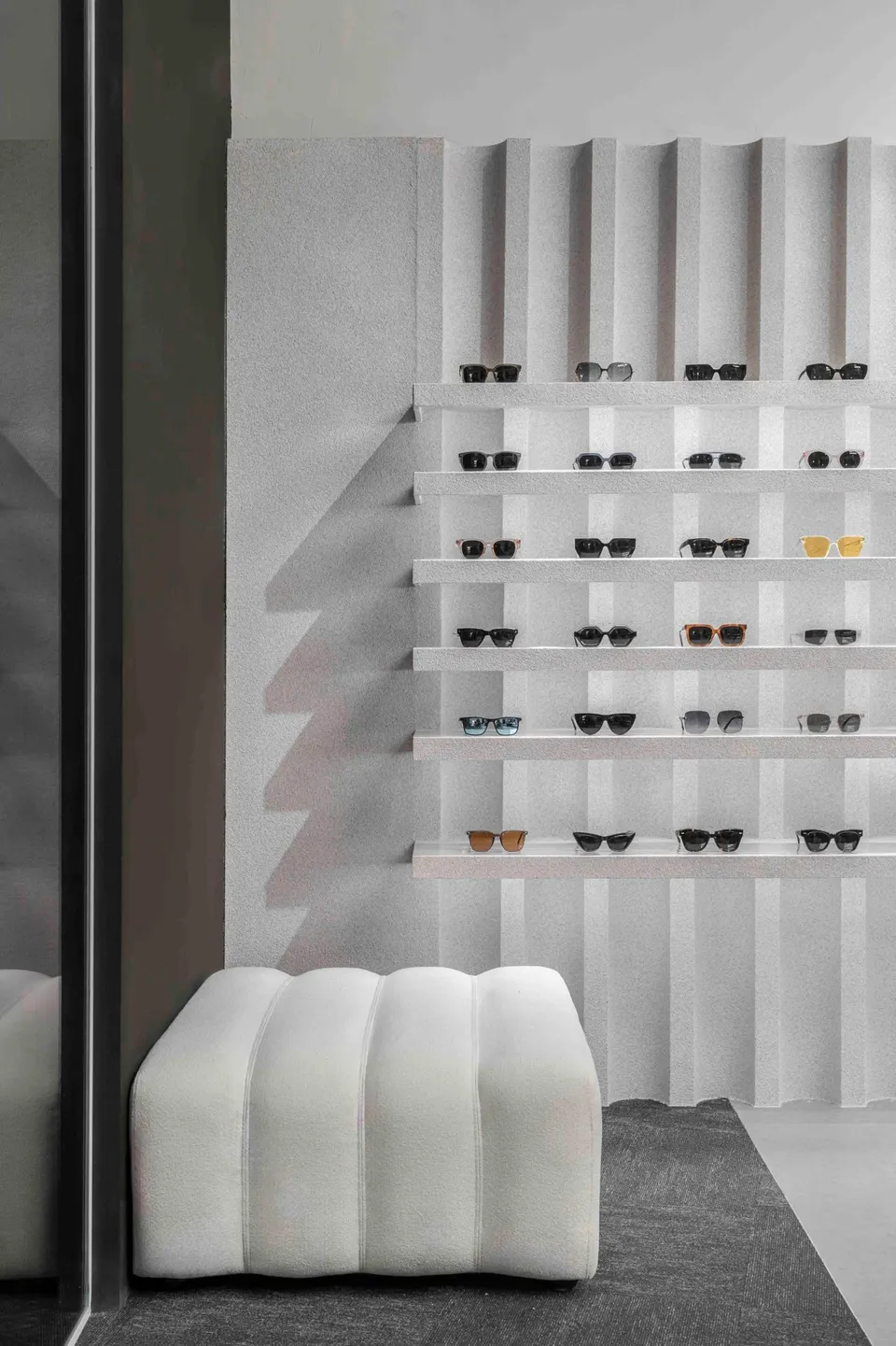 Fluted plaster wall with shelves of sunglasses and a white ottoman