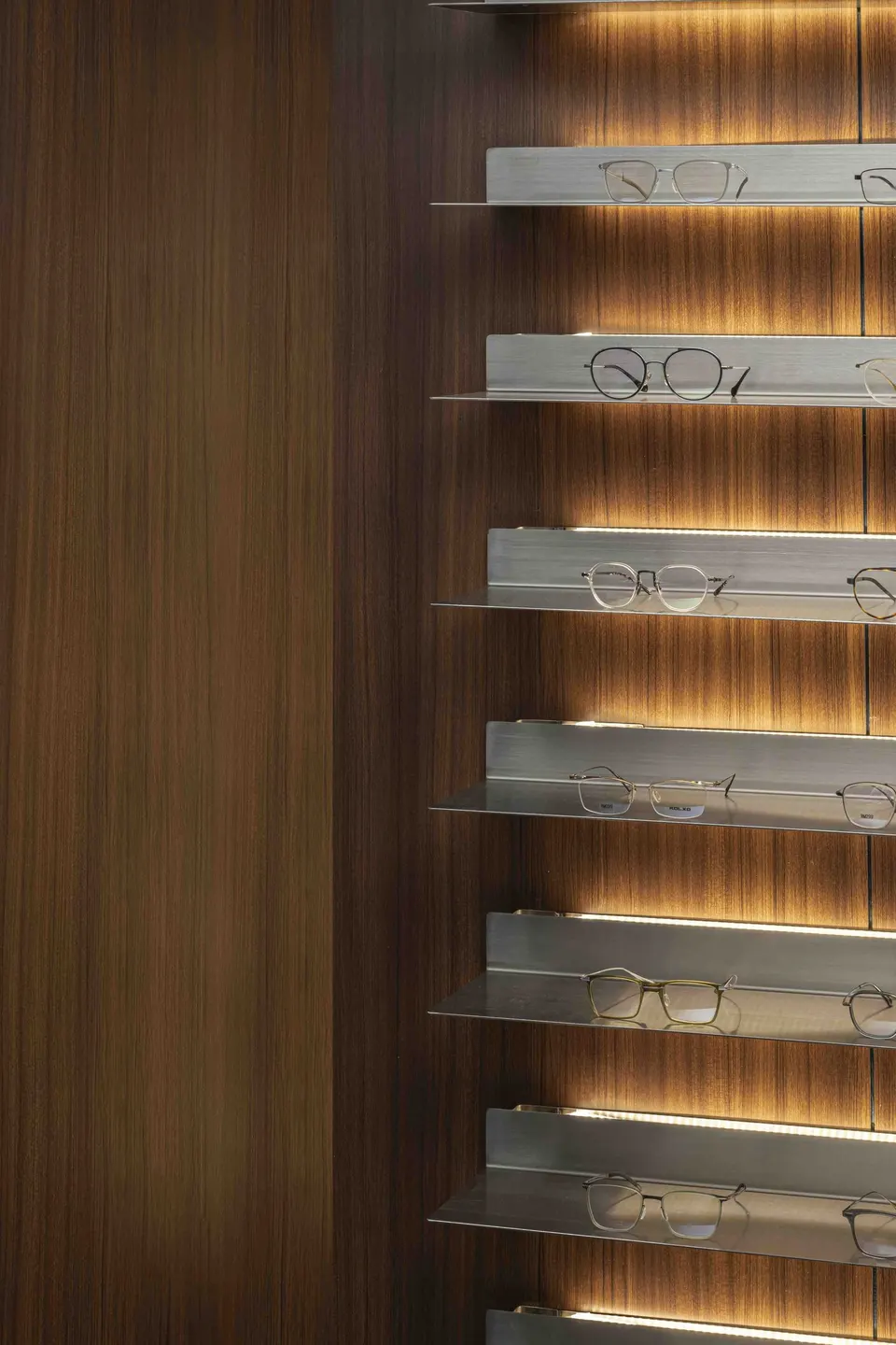 Backlit steel shelves of spectacle frames against walnut panelling