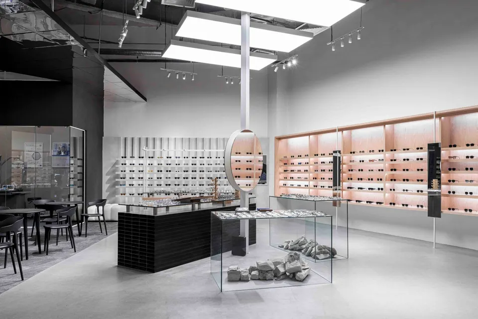 Bright sunglasses floor with glass display tables, a round hanging mirror and pale timber wall shelving